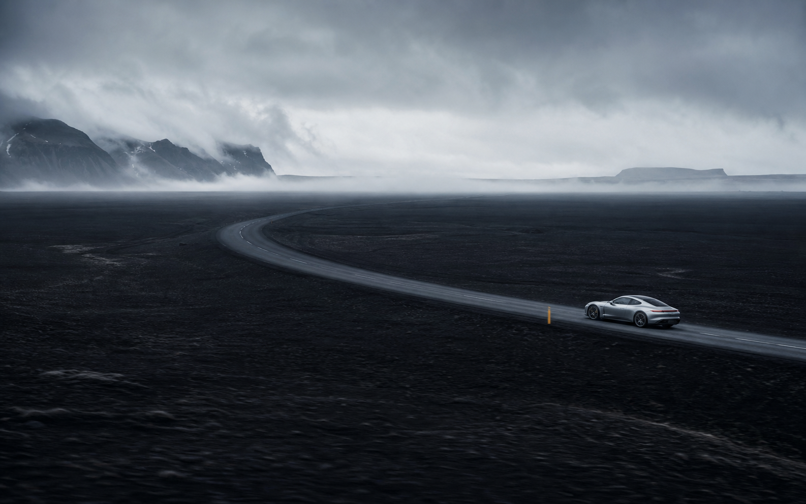 A silver car crossing a vast volcanic landscape